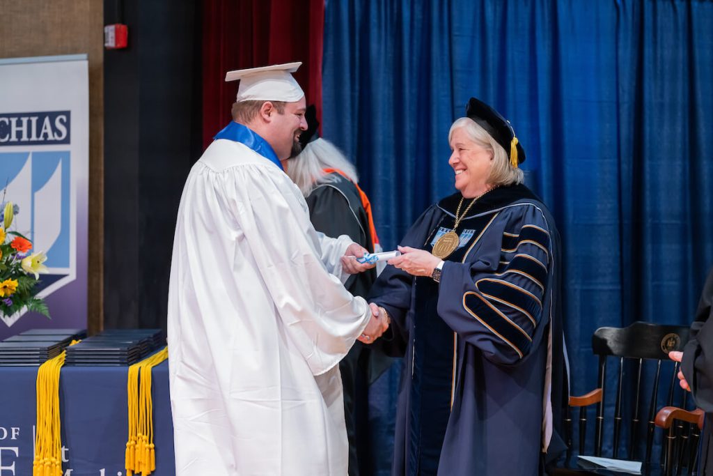 A photo of a UMaine Machais graduate receiving a diploma from President Ferrini-Mundy