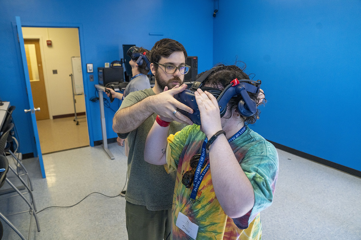 Photo of a graduate research assistant from the Immersive Mathematics in Rendered Environments Lab at the University of Maine working with an undergraduate student.