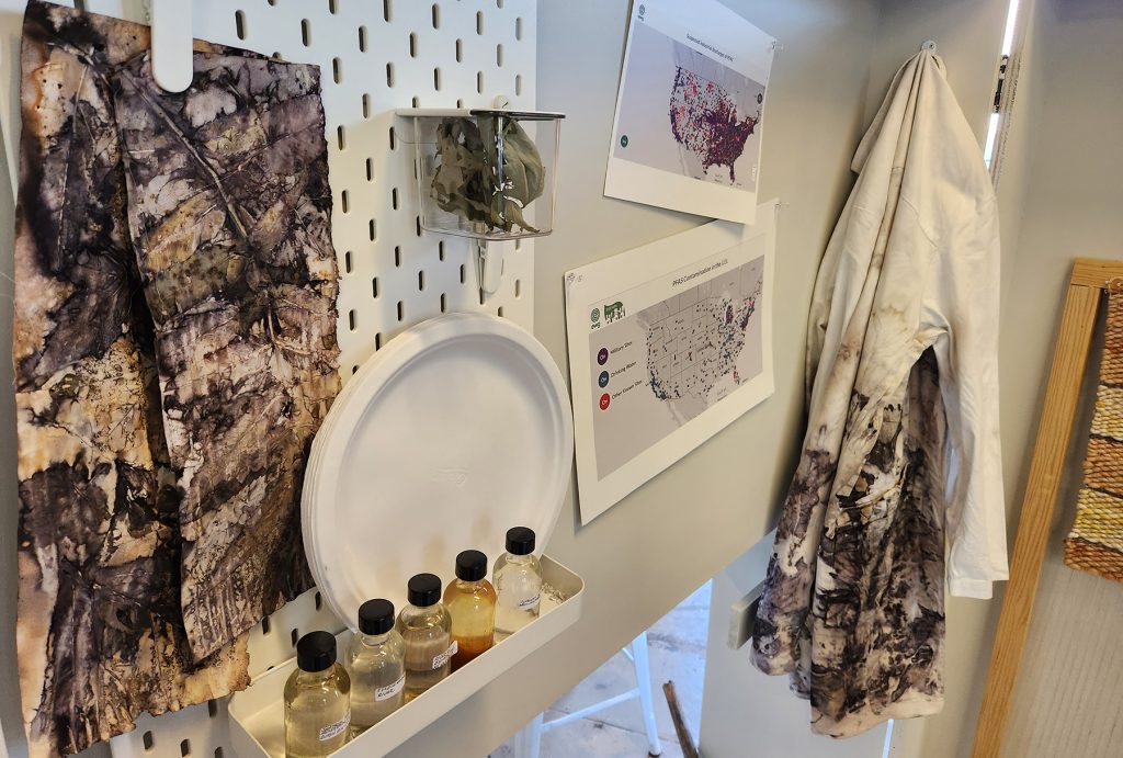 A closeup of the "Radical Gardening" exhibit featuring textiles, maps, vials of water and sediment, and paper plates.